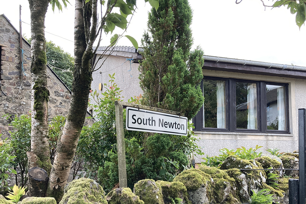 A sign that says "South Newton", in the background is Lomas, (a large bungalow)