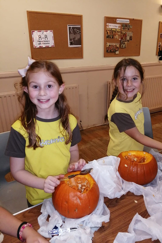 Two Brownies smiling at the camera while carving their pumpkins