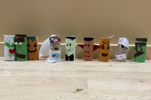 Several painted toilet rolls lined up on the floor. They are painted like mosters such as Frankenstein and pumpkins.