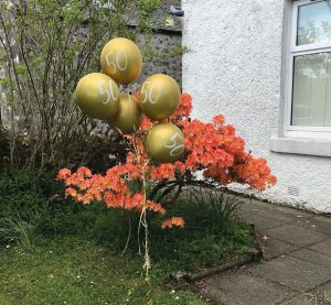 Around five gold balloons with "50" on them, displayed in a garden